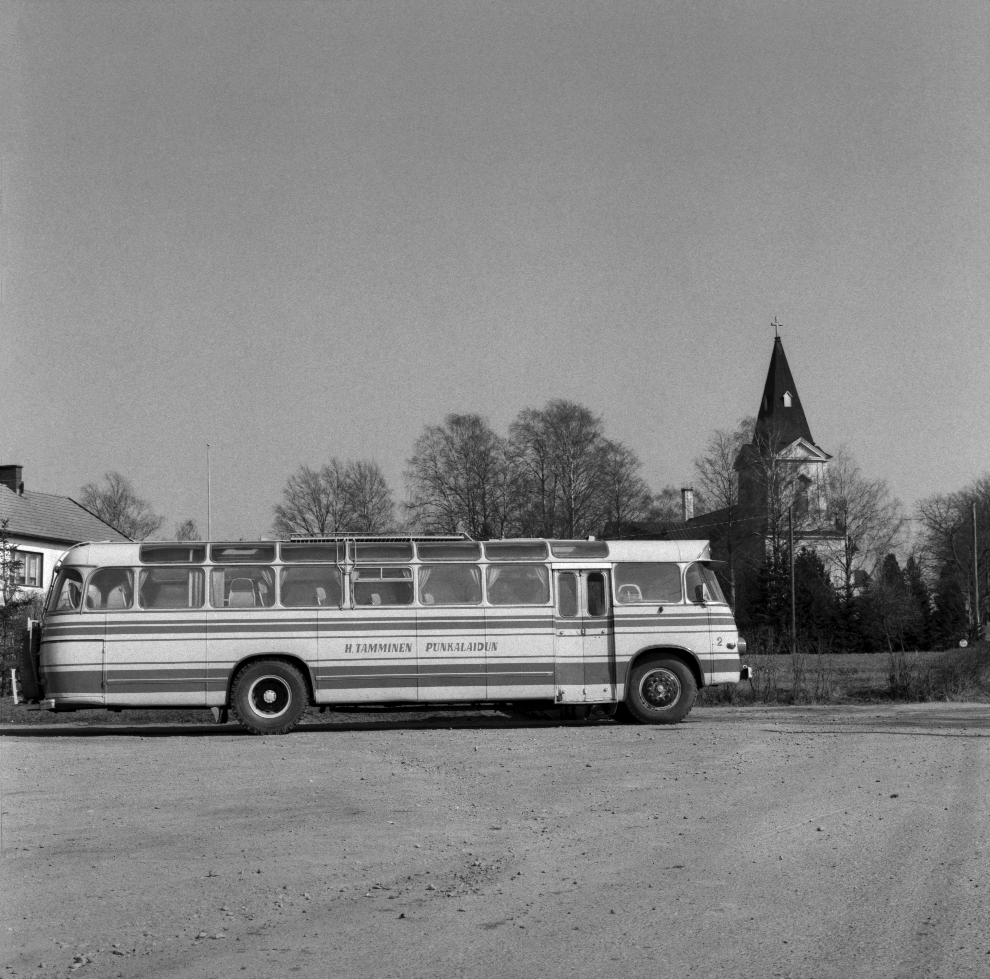Mustavalkoinen valkokuva Tammisen linja-autosta taustalla Punkalaitumen kirkko. Kuva vuodelta 1968.