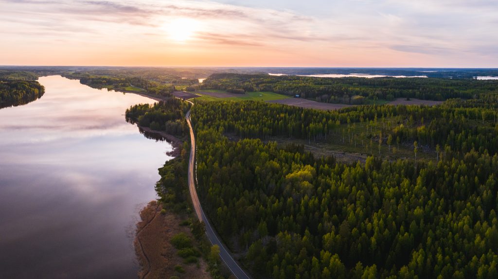 Ilmakuvaa Urjalasta auringon laskun aikaan: Rutajärvi, Taikayöntie, metsää ja peltoa. Taustalla auringonlaskun valaiseva punainen taivas, joka heijastuu veden pinnalta.
