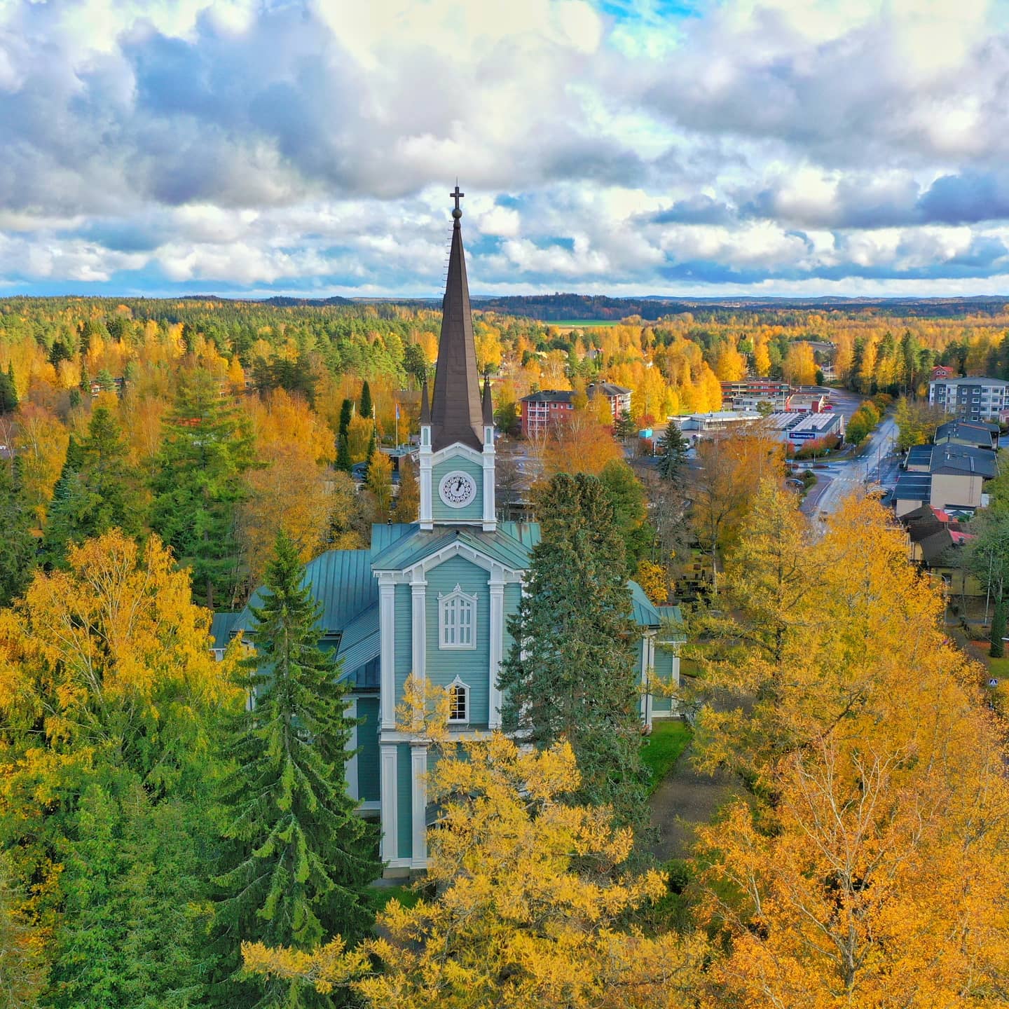 Urjalan vihreä puukirkko keltaisen ruskan värjäämän metsän ympäröimänä.