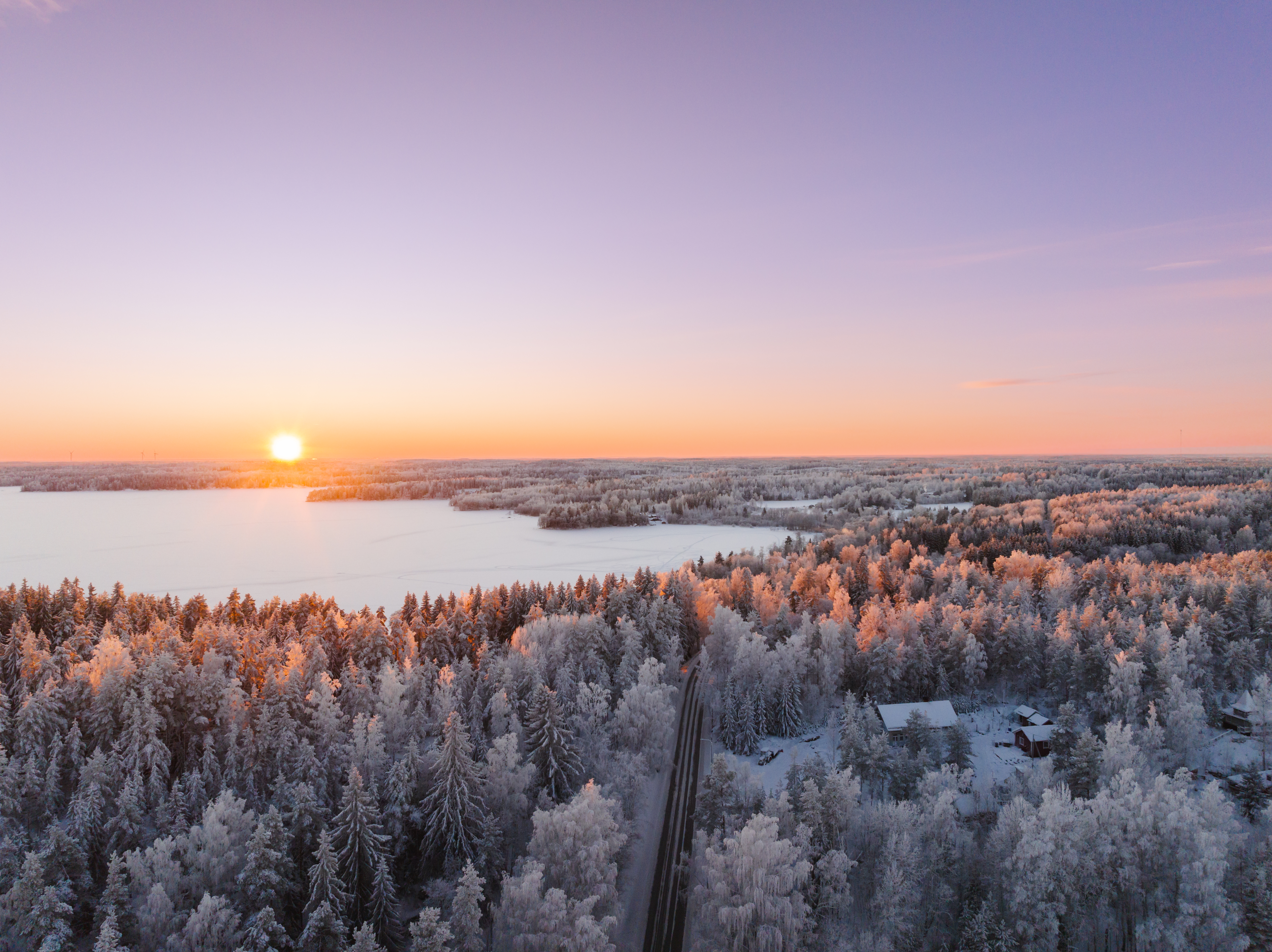 Drone-kuvaa Taikayöntien lumisista järvi- ja metsämaisemista. Taustalla pinkki taivas.